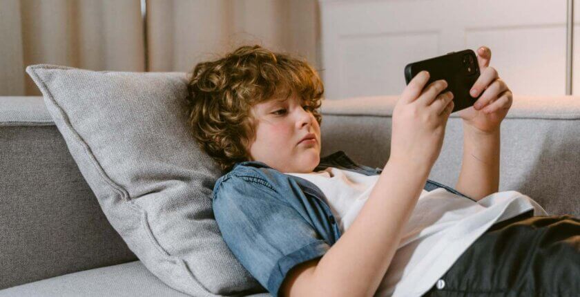 Dete gleda u telefon dok leži na krevetu